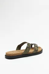 Sandalia plana negra con base de fibra trenzada y tiras cruzadas ajustables con hebillas metálicas.