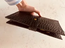 Billetera porta pasaportes de cuero sintético color marrón con textura tipo cocodrilo. Cuenta con cierre de broche y cierre de cremallera, múltiples ranuras para tarjetas y compartimentos para pasaportes y billetes.