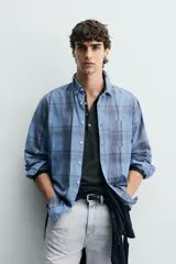 Camisa de corte regular fit confeccionada en tejido ligero de algodón, con estampado de cuadros en tonos azules y grises. Presenta cuello abotonado, manga larga con puños abotonados, bolsillo plastrón en el pecho y cierre frontal de botones.