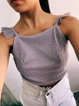 Crop top negro con textura brillante, breteles anchos con volados y espalda descubierta que se ata con lazos.