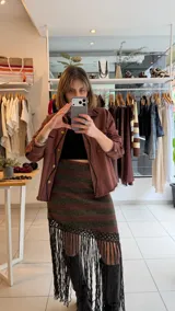 Falda tejida a rayas horizontales de corte irregular, con hilado de algodón y lúrex, y terminación de flecos tejidos a mano en crochet.