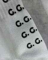 Par de medias deportivas blancas con texto 'GAINS.' en negro y agarre antideslizante con patrón de puntos 'G.G.' en la planta del pie.