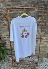 Remera azul con efecto lavado, de corte holgado y manga corta. Estampa trasera con la frase "Cherry Season" y un diseño pixelado de cerezas.