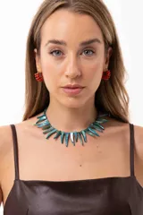 Collar corto compuesto por bastones de nácar teñidos en tono azul verdoso y mostacillas, con cierre de cadena de acero quirúrgico ajustable.