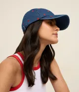 Gorra de denim azul con visera curva y pequeños corazones rojos bordados en toda la superficie. Cuenta con hebilla metálica ajustable en la parte posterior.