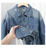Campera de jean de color azul claro con efecto gastado y roturas. Presenta cuello, cierre frontal de botones, dos bolsillos con solapa en el pecho y bolsillos laterales a la altura de la cintura.