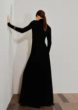 Vestido largo de fiesta color negro, con cuello alto, manga larga y diseño evasé. Presenta un corte en pico en la cintura y forro interior.
