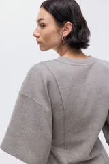 Top de punto fino color gris, con cuello redondo, hombros caídos, mangas al codo y costuras decorativas verticales en el frente que le dan un bajo levemente acampanado.