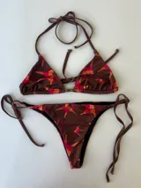 Conjunto de bikini compuesto por un top triangular con frunces y una bombacha con tiras laterales regulables. Presenta un diseño estampado con figuras abstractas en tonos marrones, naranjas y fucsias.