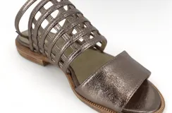 Sandalia plana color peltre, con tiras de cuero entretejidas en el empeine y pulsera con hebilla al tobillo.