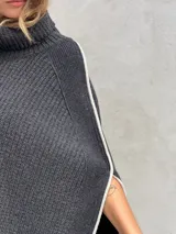 Poncho gris de lana con cuello alto y aberturas laterales con ribete blanco.