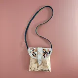 Bandolera compacta de cuero natural con solapa pintada a mano por Carolina De Cunto, correa larga negra y cierre con broche imán.