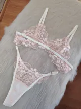 Conjunto de lencería compuesto por un bralette triangular y una bombacha tipo tanga, confeccionados en encaje floral color coral con detalles de elásticos en tono champagne.