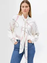 Blusa blanca hueso con estampado de cadenas en tonos negro y rosa, cuello alto con lazada ancha integrada, corte regular y manga larga.