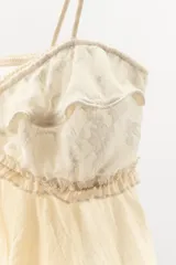 Top lencero de tirantes finos elásticos y escote en pico, confeccionado con tejido semitransparente en tono beige. Presenta detalles de encaje a contraste en la parte superior con volados y acabado asimétrico en el bajo.