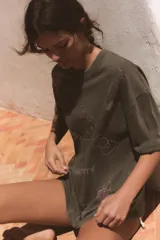 Remera oversize de color marrón grisáceo con efecto lavado, cuello redondo y manga corta. Cuenta con múltiples aplicaciones de brillos con motivos de Hello Kitty, estrellas, cerezas y moños.