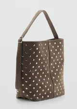 Bolso tipo hobo de cuero gamuzado color marrón, con diseño de tachas metálicas plateadas distribuidas por toda la superficie. Cuenta con una correa de hombro integrada y cierre superior.
