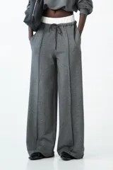 Pantalón de tiro medio color gris oscuro con efecto brillante o tweed, de corte ancho y pierna recta. Presenta doble cintura elástica con cordón de ajuste oscuro y pinzas delanteras marcadas.