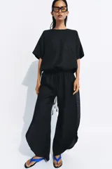 Pantalón de tiro medio confeccionado en lino, con cintura elástica ajustable mediante cordones. Presenta un diseño de pierna ancha con bajo redondeado y aberturas laterales.