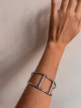 Brazalete rígido plateado con diseño geométrico de tres rectángulos unidos.