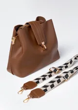 Cartera marrón de cuero sintético con tres compartimentos, cierre y correa con estampado geométrico en blanco y negro.