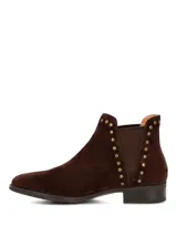 Botines de gamuza color marrón oscuro con diseño tipo chelsea, detalle de tachas metálicas a lo largo del elástico lateral y suela de goma con tacón bajo.