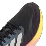 Championes de running Adidas Pureboost 5, color negro con detalles en blanco y entresuela con degradado de color que va del violeta al amarillo. Presentan parte superior de malla transpirable, cierre de cordones y suela Adiwear para mayor tracción.