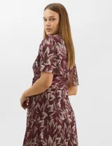 Vestido largo de fiesta con diseño cruzado, escote en V y drapeado lateral en la cintura. Presenta mangas cortas acampanadas y falda amplia con caída fluida. Confeccionado en tejido liviano con acabado plisado y estampado floral metalizado.