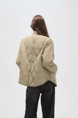 Campera acolchada de poliamida en color beige, con diseño de costuras en rombos, cuello alto, cierre frontal y bolsillos delanteros con solapa.