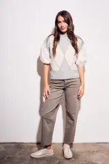 Chaleco de tejido de punto con diseño de rombos en tonos gris claro y blanco. Presenta mangas abullonadas de tela blanca con detalles de encaje y cuello redondo.