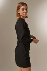Minivestido negro de poliéster con mangas largas, cuello redondo con tachas plateadas, frunces laterales y corte ajustado.