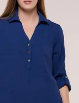 Blusa verde de calce holgado y caída fluida, confeccionada en tejido tipo crepé. Cuenta con cuello camisero con solapa, escote en V y cierre parcial al frente con tres botones metálicos. Las mangas son largas con puños abotonados.