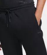 Pantalón deportivo de corte jogger, color negro, con cintura elástica ajustable mediante cordón, bolsillos laterales y puños acanalados en los tobillos. Confeccionado en tejido de algodón con interior felpudo.