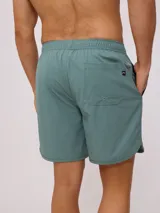Short de baño tipo volley color verde azulado, con cintura elástica y cordón de ajuste en color azul marino. Presenta un parche con el logo de la marca en la pierna izquierda y aberturas laterales en el ruedo.