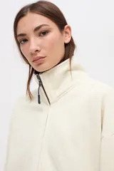 Campera oversize de felpa con friza, color crudo, con cierre metálico frontal, cuello alto y bolsillos laterales amplios. Presenta detalles de cortes en mangas y hombros, y bordado decorativo.