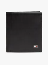 Billetera plegable en tres partes de cuero negro con textura acanalada. Presenta un logo esmaltado de la marca en la esquina inferior derecha. Incluye compartimentos para billetes, ranuras para tarjetas y un bolsillo para monedas.