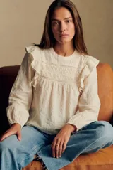 Blusa de color arena con diseño de volados en los hombros, detalle de fruncido en el pecho y mangas largas con puños elásticos.