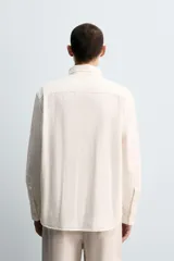 Camisa de corte relajado confeccionada en tejido de algodón, con cuello solapa, manga larga con puños abotonados, bolsillo frontal en el pecho y cierre de botonadura.