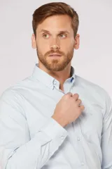 Camisa sport lisa de corte clásico, confeccionada con tejido elástico con spandex para mayor comodidad. Presenta cuello camisero con botones, mangas largas con puños abotonados y un bolsillo frontal en el pecho con logo bordado.