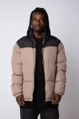 Campera puffer de diseño bicolor, con cuerpo en tono beige y canesú superior en color negro. Presenta cuello alto, cierre frontal completo y puños elásticos.