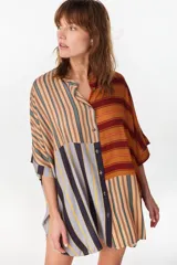 Vestido camisero corto con diseño de paneles combinados en distintos patrones de rayas verticales y horizontales, en tonos rojo, azul, beige y blanco. Posee cuello mao, cierre frontal con botones y mangas cortas caídas.