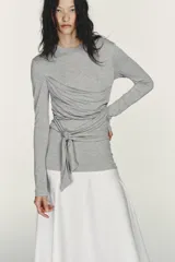 Vestido midi de cuello redondo y manga larga, con la parte superior gris y la falda blanca. La parte superior presenta un detalle de tejido superpuesto ajustable con lazada en la cintura. La falda es de tipo gabardina.