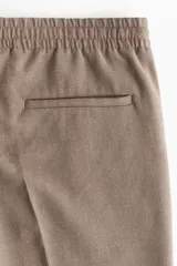 Pantalón de corte relajado y pierna recta, confeccionado en tejido suave de color marrón. Presenta cintura elástica con cordón de ajuste, pliegues frontales y traseros, bolsillos laterales y un bolsillo posterior insertado.