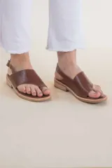 Sandalias de cuero color marrón, con tira ancha sobre los dedos, tira trasera con hebilla y suela plana.