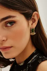 Aro de estilo étnico con piedra rectangular verde central, engarzado en metal dorado y decorado con pequeñas cuentas colgantes en la base.