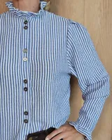 Camisa de manga larga con estampado de rayas verticales en tonos crudo y beige. Presenta cuello alto con volados, cierre frontal con botones dobles y puños con volados.