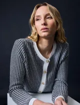 Cardigan de tejido tweed celeste y blanco, con escote redondo, cierre frontal con botones metálicos dorados y bolsillos simulados en el frente.