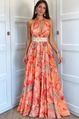 Vestido largo sin mangas con escote halter cruzado y choker integrado. Presenta un diseño fluido con estampado multicolor en tonos anaranjados, fucsias y celestes, falda amplia y larga, acompañado por un cinturón claro con apliques florales.