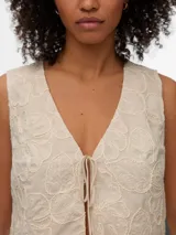 Chaleco color beige con diseño bordado, escote en V y cierre frontal con finos lazos para atar.