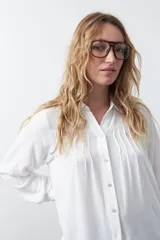Camisa de manga larga color blanco, con cuello camisero y detalle de alforzas verticales en el frente. Presenta un calce relajado y cierre frontal con botones.
